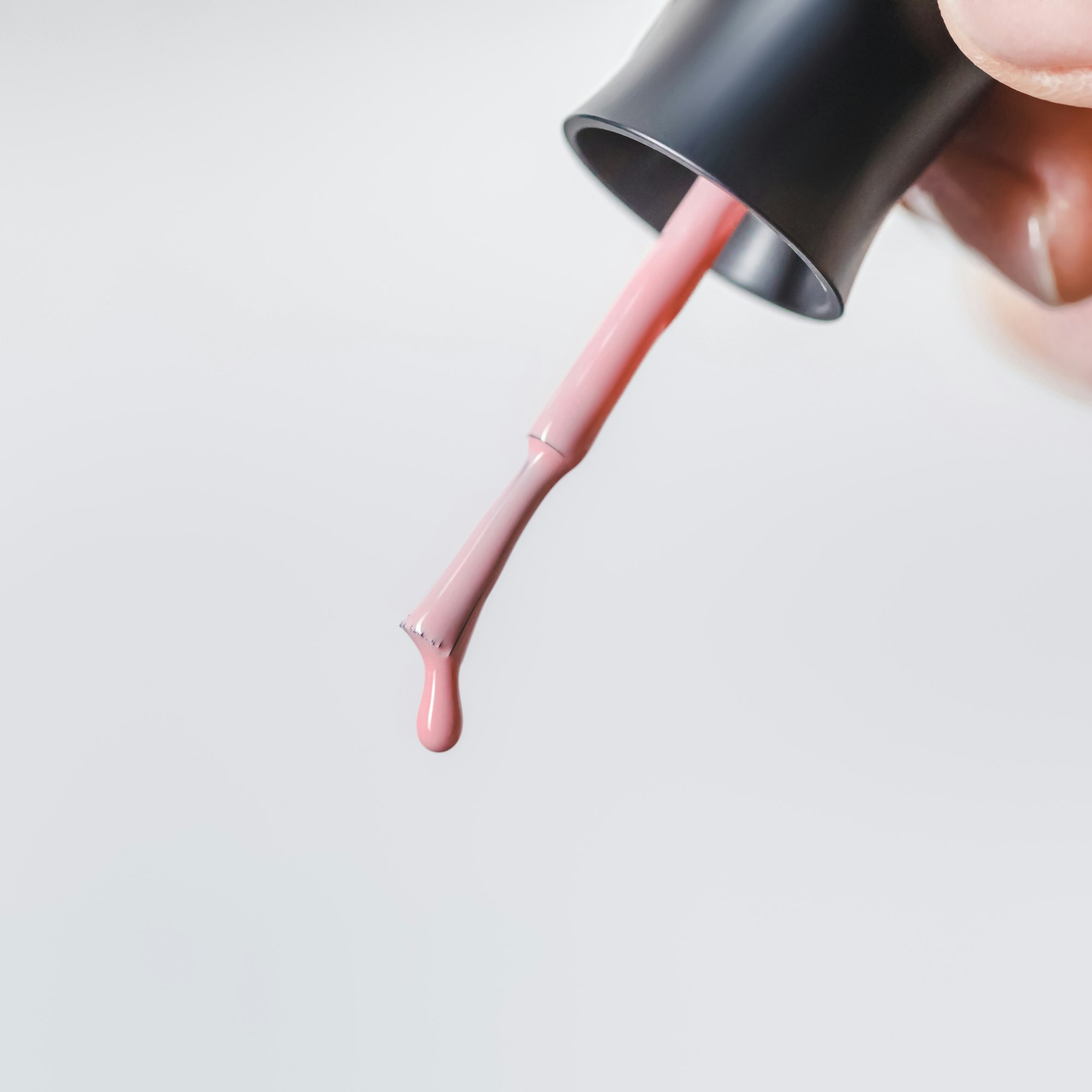 partial view of woman holding brush with pink dripping nail polish isolated on grey
